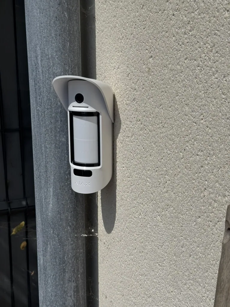 Détecteur extérieur bi-technologie posé sur la façade d'une maison